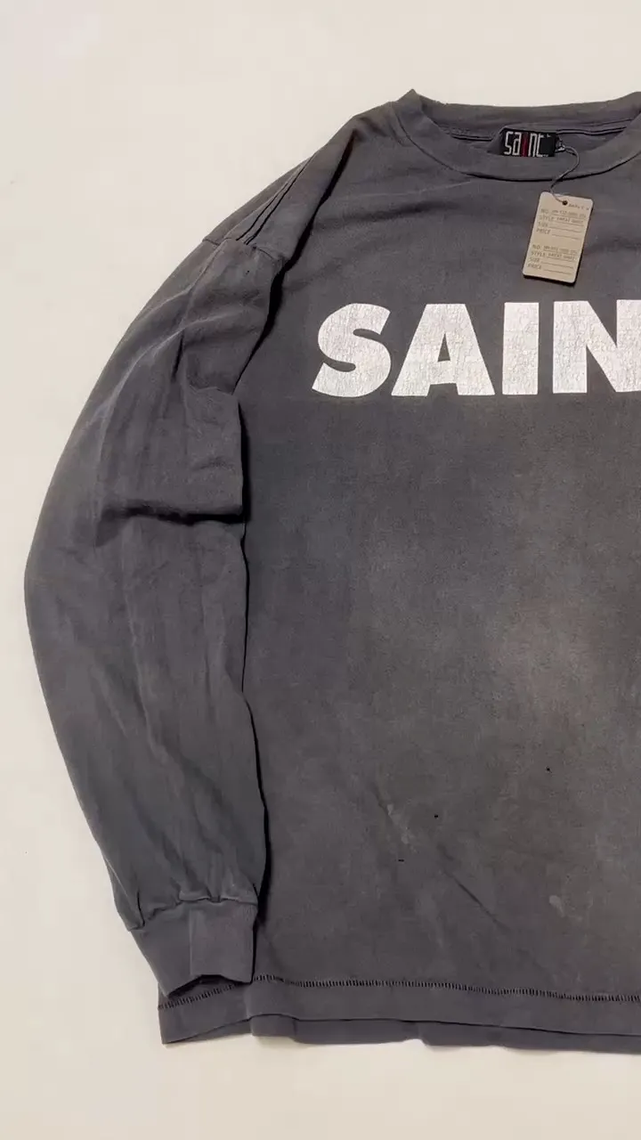 SAINT Mxxxxxx S>N>T LS TEE/BLACK Autumn and winter new style S>N>T slogan crack printed long TEE, washed black S-XL Asut ready-made garments dyed, the whole piece sprayed with horse-hair spray, and then sprayed again to fade the color. The collar and cuffs are frayed. Many hangings are worn NEW VINTAGE. Heavy craftsmanship.